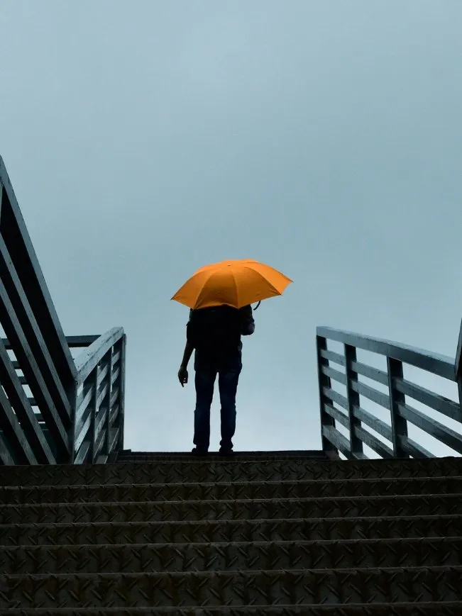 Silhouette avec un parapluie orange en haut d'un escalier